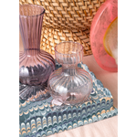 Pink glass vase on a decorative tray with a woven basket in the background