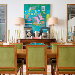 Pair of celadon green twisted taper candles in brass candle holders on wooden dining table with green velvet chairs.
