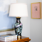 Decorative lamp with floral design on a wooden surface, books, and framed artwork in the background.