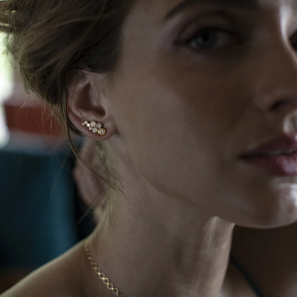 Close-up of a woman wearing gold diamond cluster earrings and a necklace.