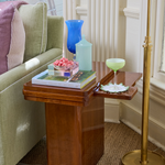 Set of 6 brown wooden wave-shaped coasters on a side table, one holding a glass and a pink flower arrangement.