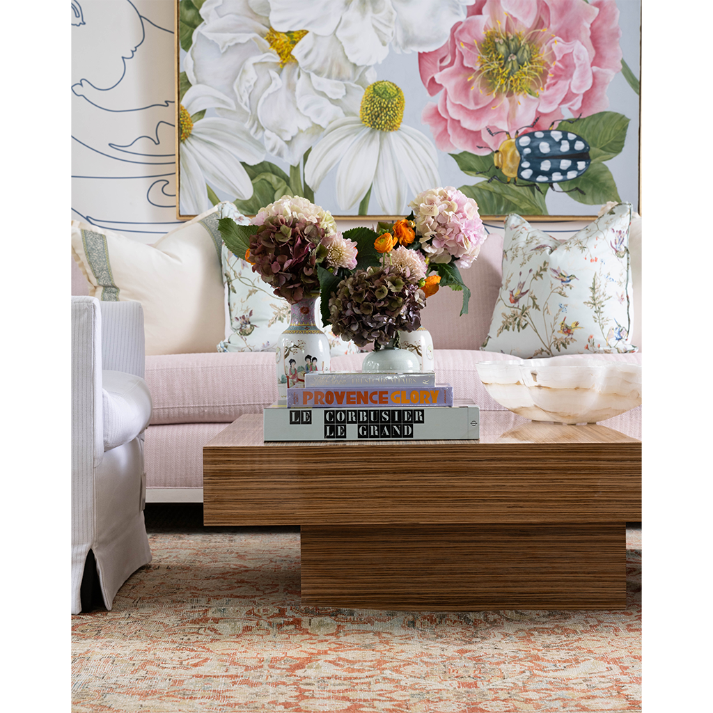 Rectangular wooden cocktail table with a thick, layered design and clean lines, styled with stacked books and floral.