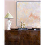 A framed abstract wall art print hangs above a dark wood console table in a styled interior. The artwork features soft pastel washes of beige, cream, and peach with a coral-like textured accent.