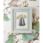 A framed botanical art print featuring a striped cactus with yellow flowers, set against a patterned wallpaper with matching green and beige illustrations.