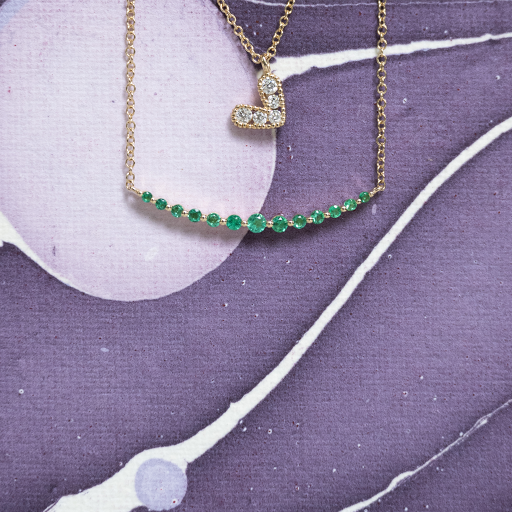 Necklace with a heart-shaped pendant and green gemstones on a purple and white abstract background