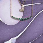 Necklace with a heart-shaped pendant and green gemstones on a purple and white abstract background