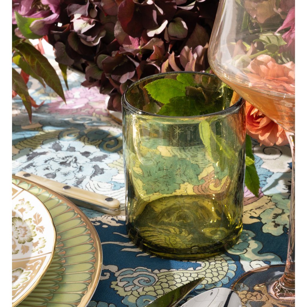 Green glass on a patterned tablecloth with flowers and cutlery in the background