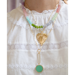 A gold-tone layered necklace with a textured sunburst pendant, a white pearl, and a mint green oval pendant, displayed on a white lace-trimmed fabric.