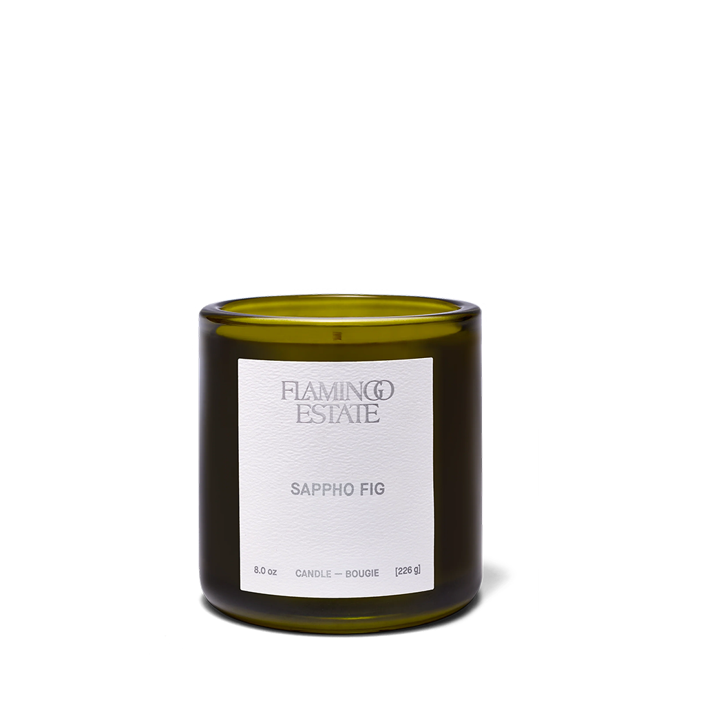 A Flaming Estate 'Sappho Fig' scented candle in a dark olive-green glass jar with a white paper label, set against a plain white background.