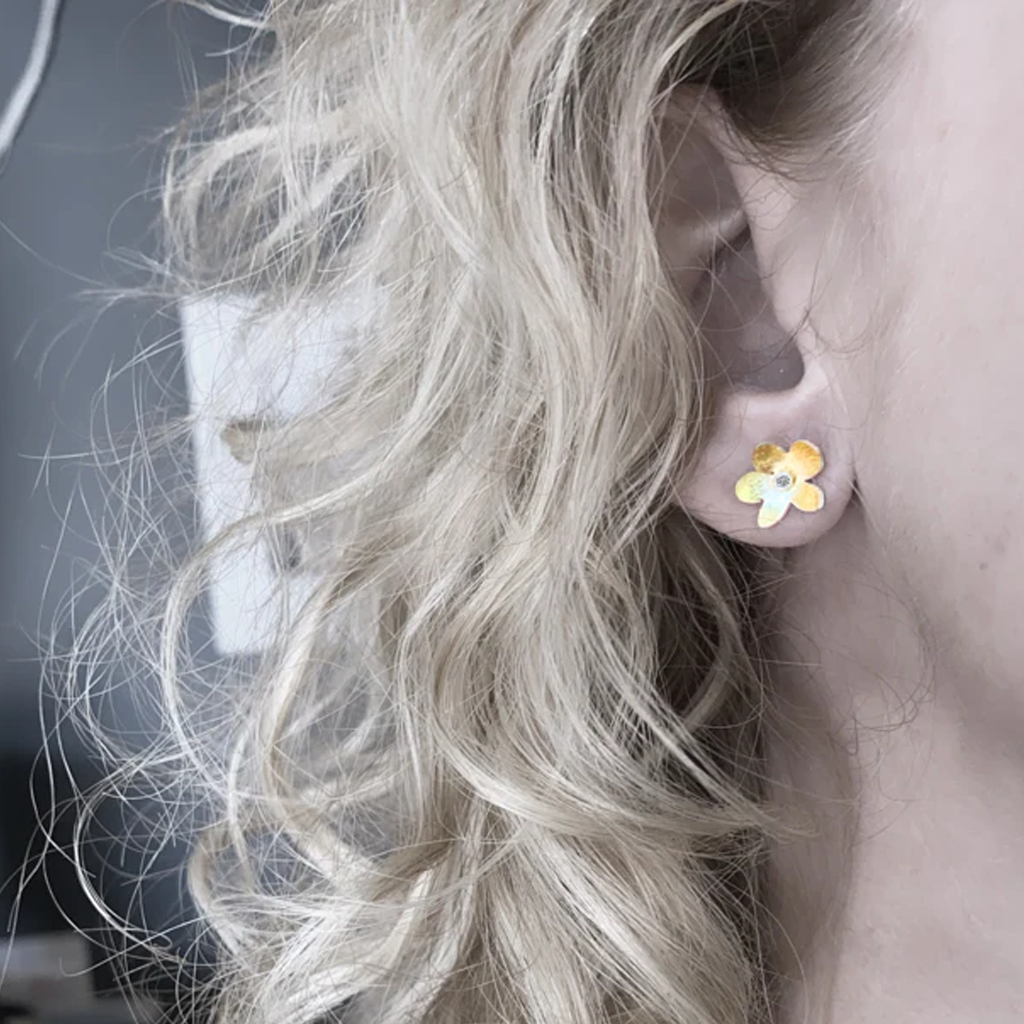 Close-up of a person wearing a floral gold earring with blonde hair.