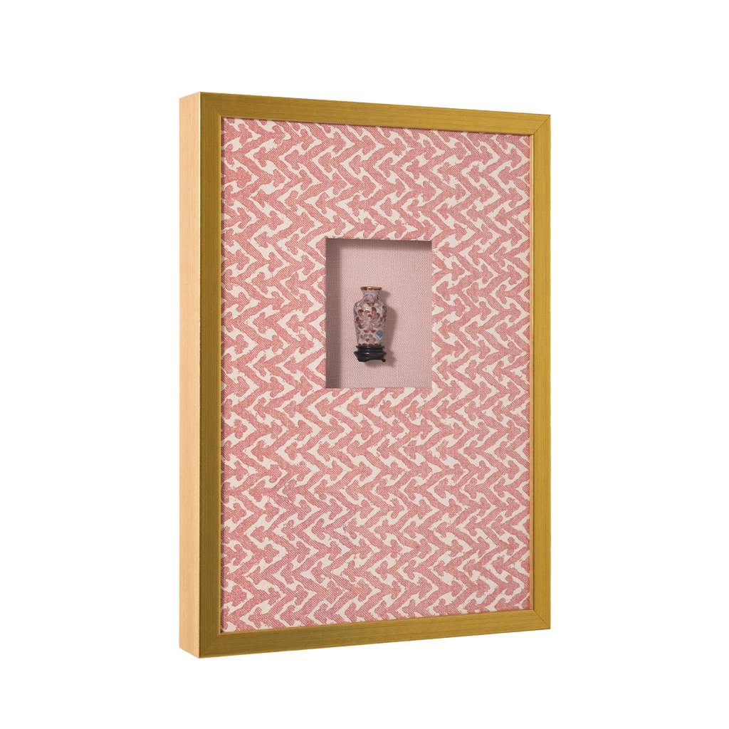 Gold-framed shadow box with pink geometric patterned background and a miniature cloisonné vase centered inside.