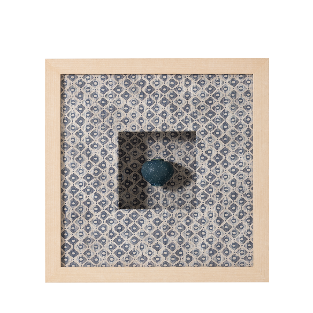 Decorative item with a blue sphere on a patterned fabric background inside a wooden frame.
