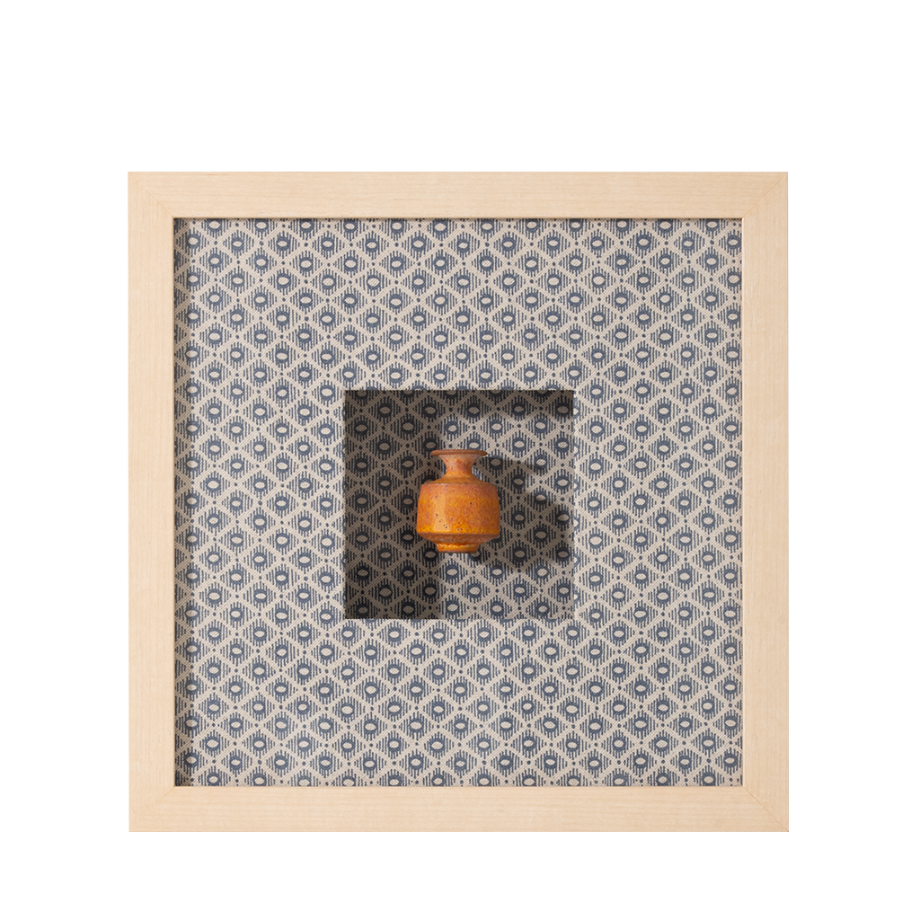 Small wooden vase on a patterned fabric background with a wooden frame.