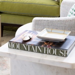 Book titled 'Mountain House' on a marble table with a decorative plate on top, in a living room setting.