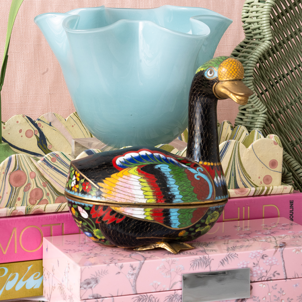 Decorative goose with colorful patterns on a pink surface with books and a blue bowl.