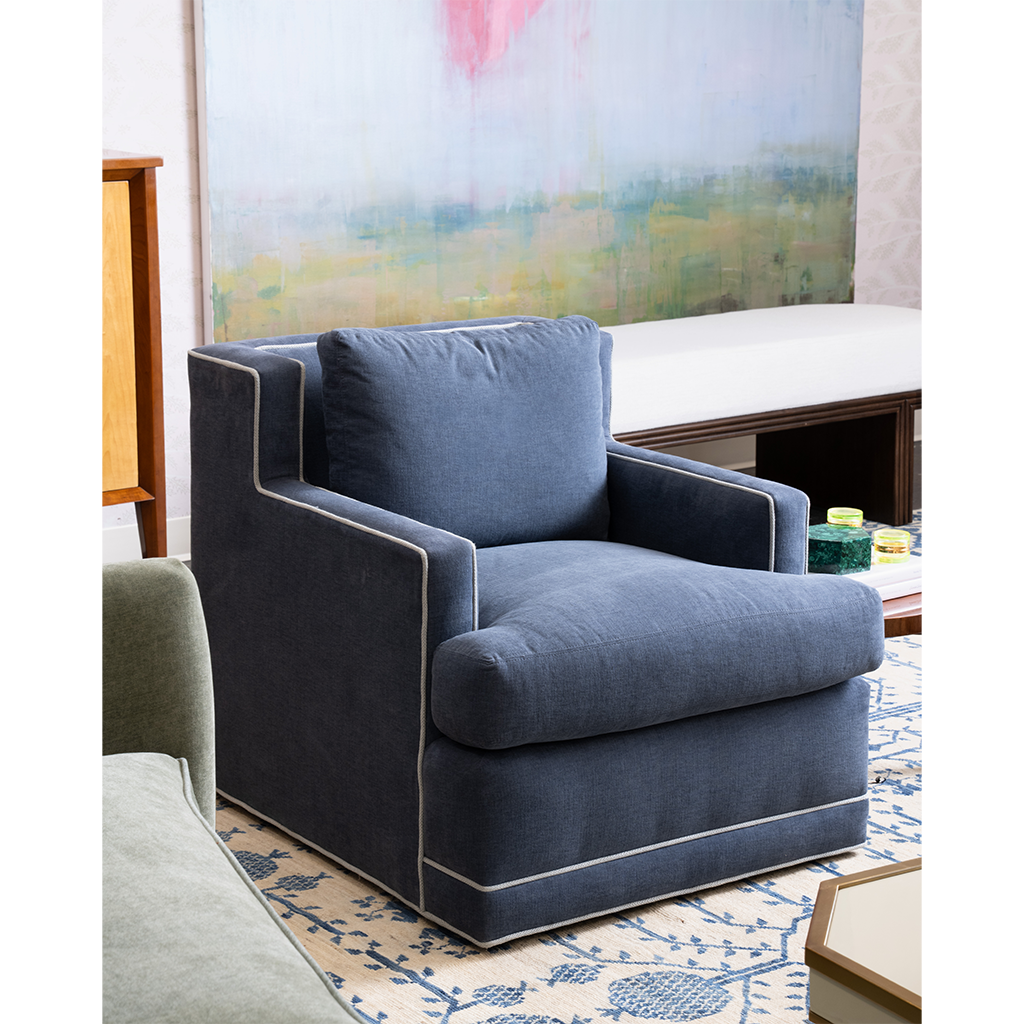 A dark blue swivel chair with white piping with artwork in the background
