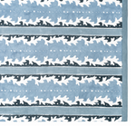 A close-up of a textile showing a repeating horizontal pattern with white abstract leaf-like motifs on a dusty blue background, bordered by a solid blue edge.