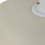 Close-up detail of a light fixture showing a large matte beige shade, a white circular base, and a small brass-toned accent.