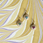 Three gold heart-shaped pendants with colored stones on a yellow background
