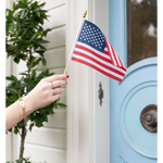 Delicate gold bracelet with "I Love You" engraved script on a wrist holding a small American flag.