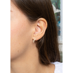 A close-up side view of a person's ear wearing a small gold-toned cross-shaped stud earring.