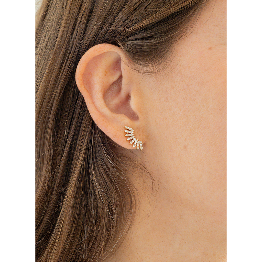 A close-up of a person's ear wearing a small gold leaf-shaped stud earring with clear stones.