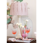 White ceramic table lamp with pleated pale pink fabric shade on floral-themed background.