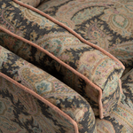 Close-up of upholstered armrests with a detailed paisley pattern in muted beige, brown, and teal tones, accented by a contrasting dusty rose pink piping.