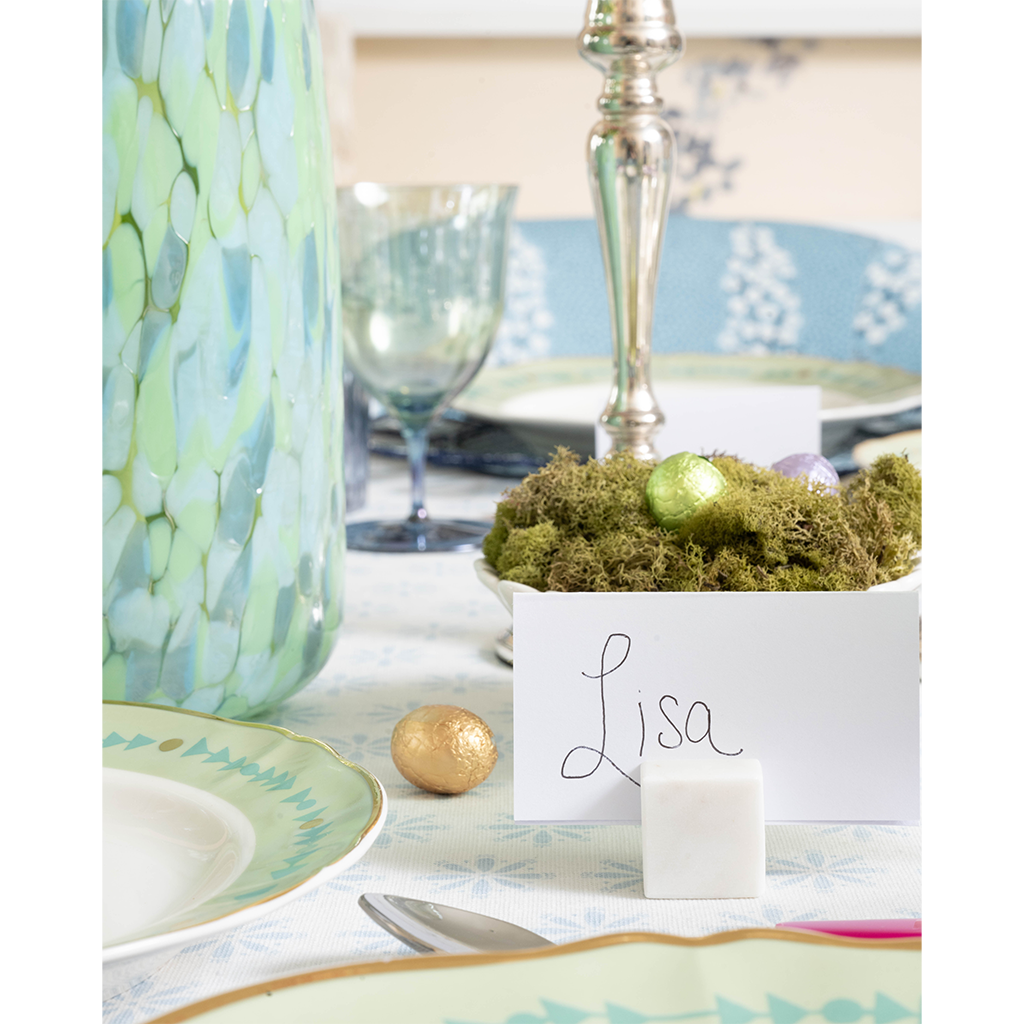 White marble place card holder with handwritten "Lisa" card on a decorated tabletop.