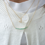 Two gold necklaces with a heart pendant and green gemstones on a white sweater.