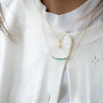 Gold necklace with green gemstones worn by a person in a white sweater.