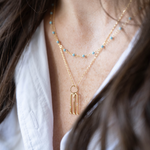 Layered gold necklaces with keyhole pendant and delicate blue stone beads on fine gold chain.