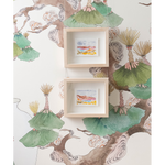 Two small framed watercolor art prints hang on a wall against a decorative wallpaper featuring green ginkgo leaves and brown tree branches.