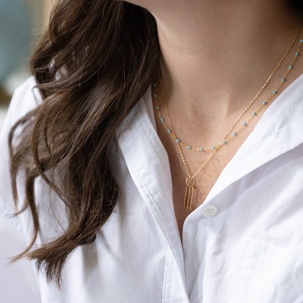 Delicate gold chain necklace with a small keyhole pendant worn over a white button-up shirt.