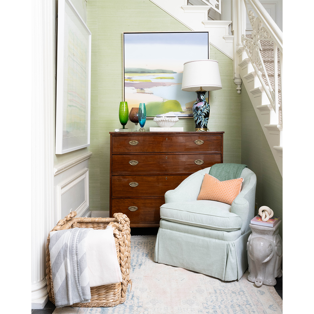 Interior with accent chair, chest topped with vases and lamp, a basket with blankets, and an elephant side table.