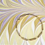 Gold bracelet on a marbled yellow and purple background