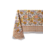 A cream-colored tablecloth with a vibrant, multicolored floral and paisley block-print pattern, draped to show its detailed border and striped fringe against a solid white background.