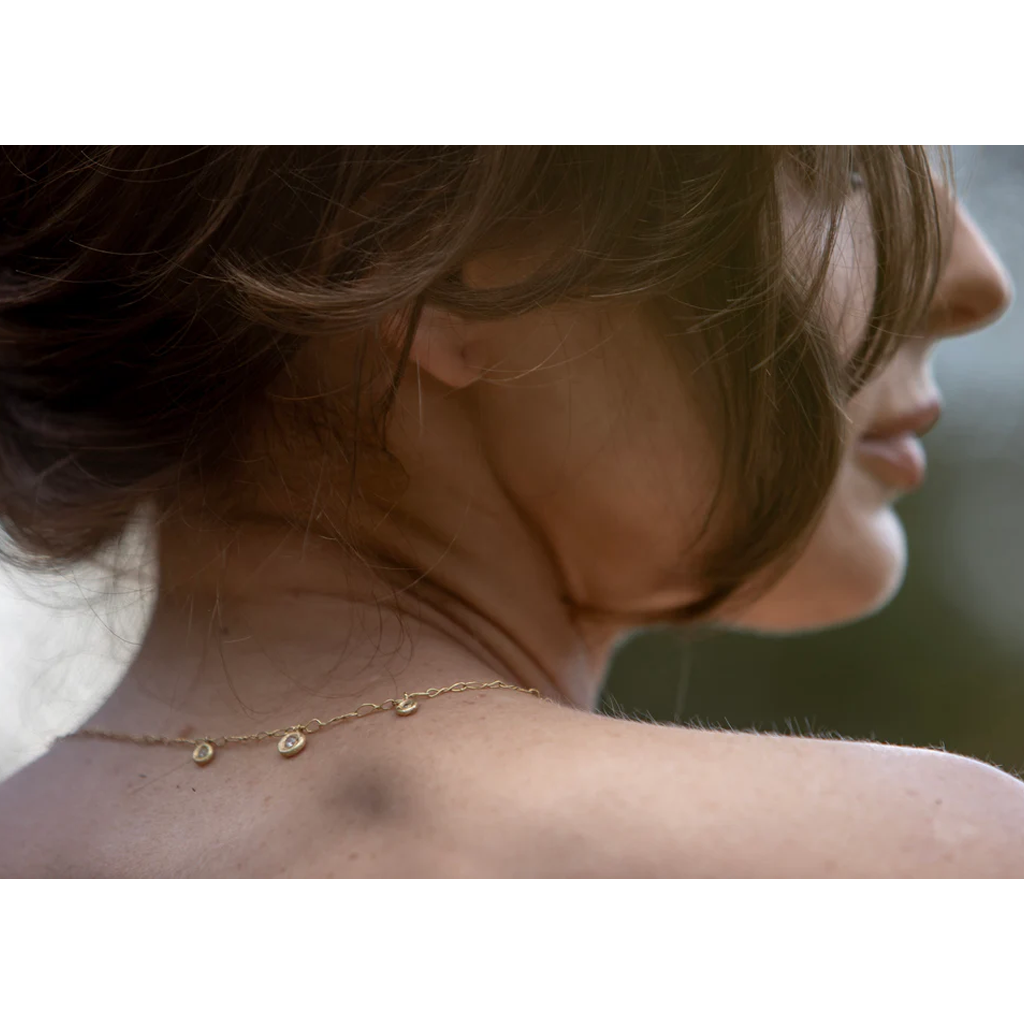 Close-up of a person wearing a delicate gold necklace with a blurred background