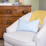 Gray armchair with a blue patterned pillow and yellow blanket in front of a wooden dresser.