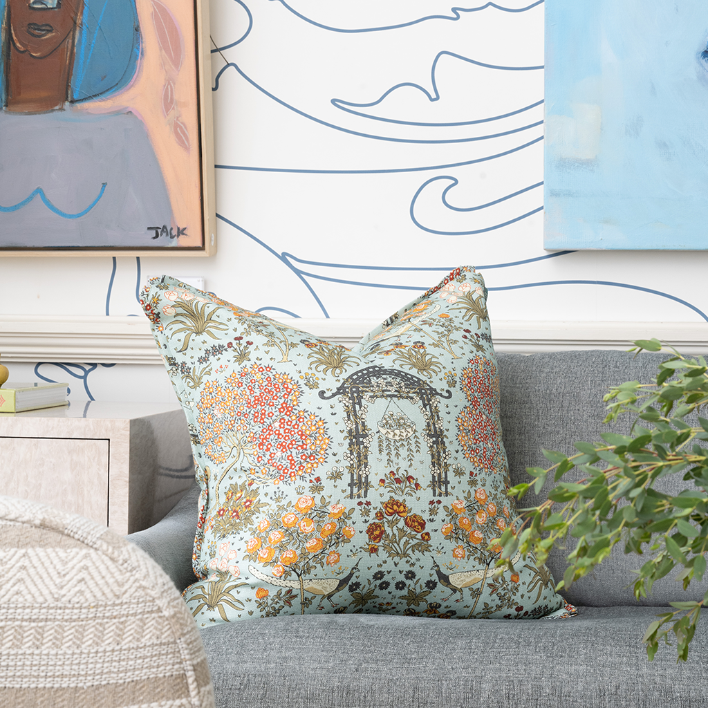 Image of a colorful patterned pillow sitting on a grey sofa in front of a blue and white wall
