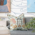 Image of a colorful patterned pillow sitting on a grey sofa in front of a blue and white wall