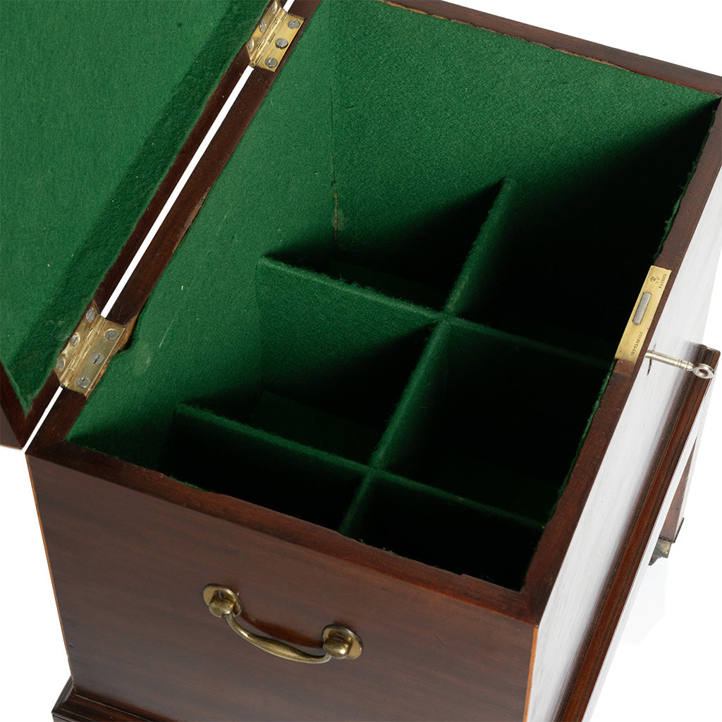 A close-up of an antique mahogany cellaret with its lid open reveals a green felt-lined interior divided into fitted compartments for storing bottles and accessories. A brass handle and locking mechanism are visible on the exterior, highlighting the piece's functional, elegant design.
