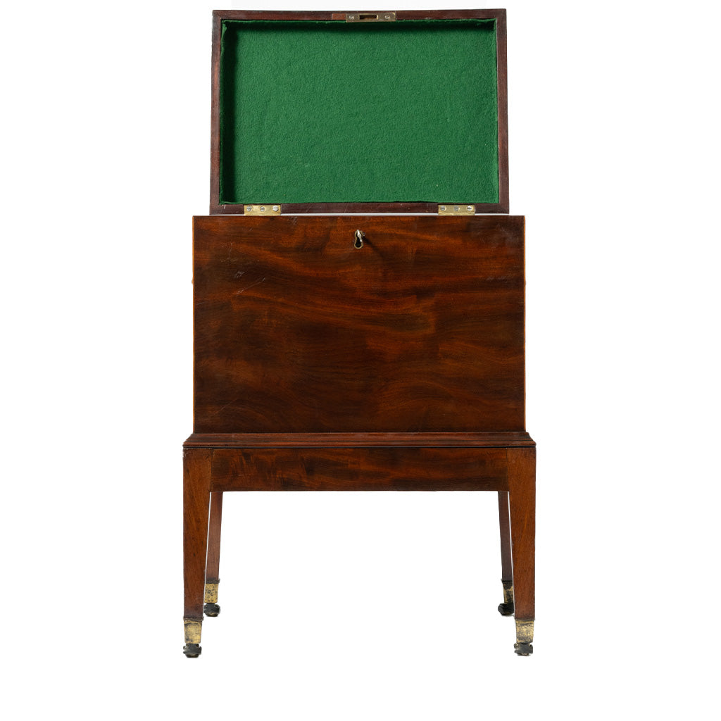 A front view of an antique mahogany cellaret with its hinged lid open reveals a green felt-lined interior designed for storing bottles. The piece stands on straight legs with brass-capped feet and features a simple, elegant design with a central keyhole on the front.