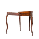 A side view of a wooden drop-leaf table shows one leaf extended, revealing its hinged construction and elegant, curved legs. The table features a warm wood finish with subtle veneer detailing and a classic antique design.