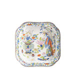 A square ceramic serving bowl features a colorful hand-painted design of flowers, bamboo, and stylized rock formations in shades of blue, green, orange, pink, and yellow on a white background. An intricate floral border frames the rim, giving the piece a vibrant, antique-inspired look.