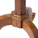 Close-up of a wooden table basewith curved legs, a central vertical post, and a brass-colored metal band around the joint, shown on a white background.