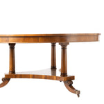 A close-up of a round wooden dining table featuring turned legs and a curved apron, shown against a plain white background.