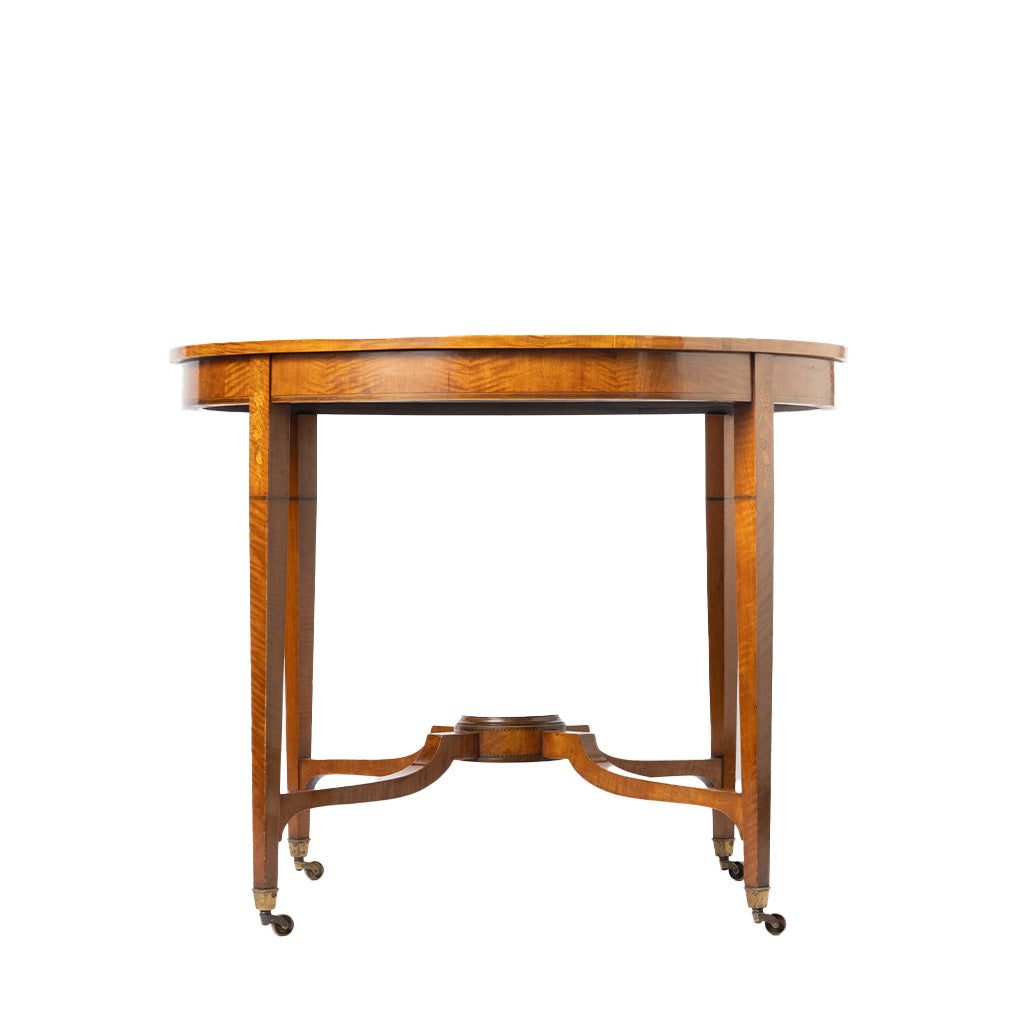 A vintage round wooden table with a warm honey-brown finish, featuring a central pedestal base and four legs fitted with brass caster wheels, shown against a plain white background.