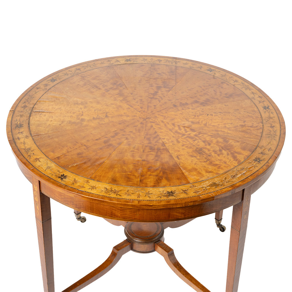 Round wooden table with a radiating inlay pattern on the top, supported by three curved legs with brass casters, shown on a white background.