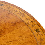 Close-up of a round wooden table showing a warm honey-brown flamed wood surface with an inlaid floral border.